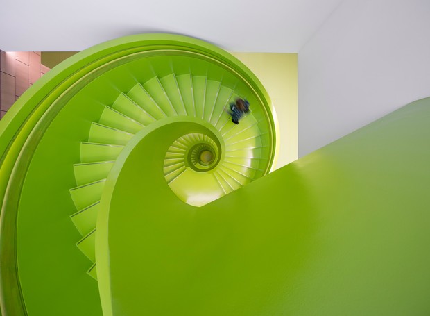 O design interior do edifício é muito mais ousado do que o exterior, com acabamentos em cores de bloco por toda parte - incluindo uma escada em espiral verde brilhante (Foto: Reprodução/Dezeen)