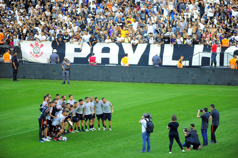 Corintianos posam para foto no gramado da Arena, com torcida ao fundo — Foto: Marcos Ribolli