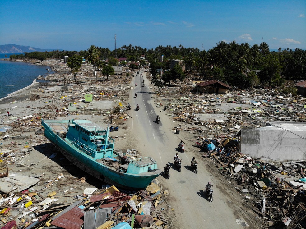 Motoqueiros passam ao lado de um barco em meio a entulhos e construÃ§Ãµes destruÃ­das em Palu, na IndonÃ©sia, apÃ³s Ã¡rea ser atingida por um terremoto e um tsunami â Foto: Jewel Samad/AFP