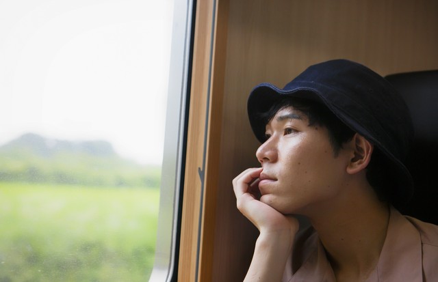 A man of millennial takes a trip by train  and is looking out of the window with being lost in thought. (Foto: Getty Images)