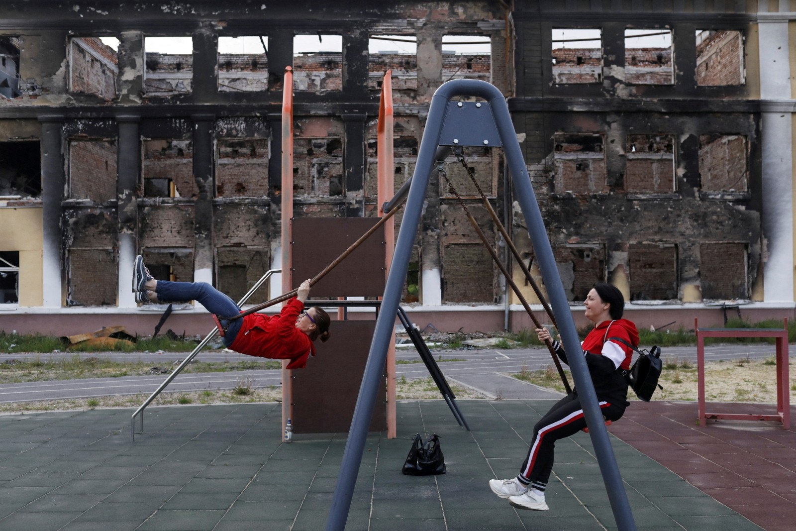Ex-alunos de uma escola usam um balanço no playground da instituição destruída, em Kharkiv — Foto: Ricardo Moraes/REUTERS 