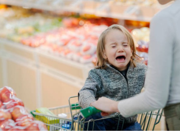 Criança acompanhada da mãe chorando em carrinho de supermercado (Foto: Getty Images)