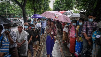 Pessoas esperam sob chuva em fila para receber refeição grátis ao longo de uma rua em Yangon, em Mianmar  — Foto: STR / AFP