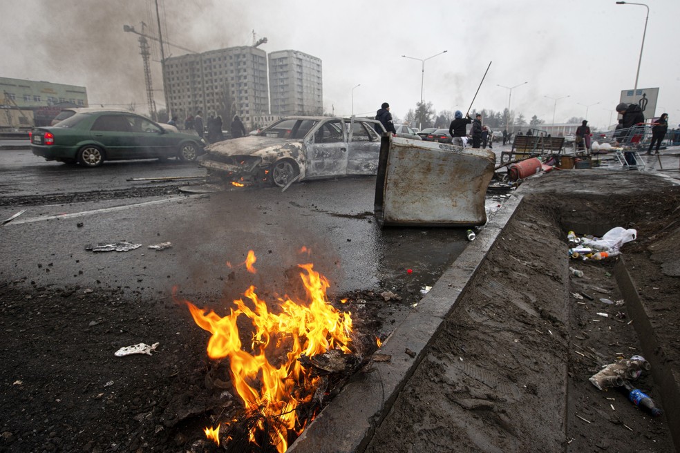 Pessoas passam por carros queimados após os confrontos em uma rua de Almaty, no Cazaquistão, na sexta-feira (7). — Foto: Vasily Krestyaninov/AP