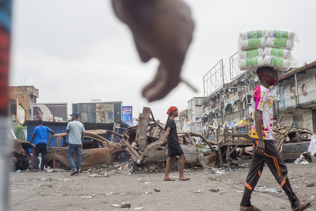 Pessoas caminham por uma barricada no mercadão de Kinshasa, na República Democrática do Congo, na terça-feira (9), quando comerciantes protestaram pela reabertura de lojas, fechadas para conter a disseminação da Covid-19. — Foto: Arsene Mpiana / AFP