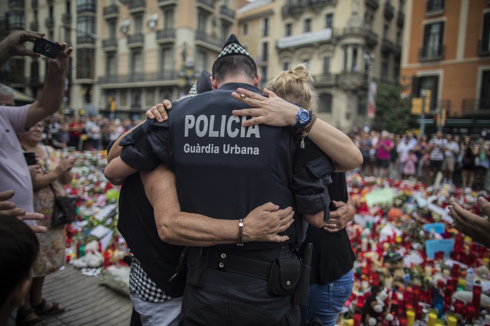 Policial abraça família em frente ao memorial em memória das vítimas do ataque em Las Ramblas, em Barcelona — Foto: AP Photo/Santi Palacios