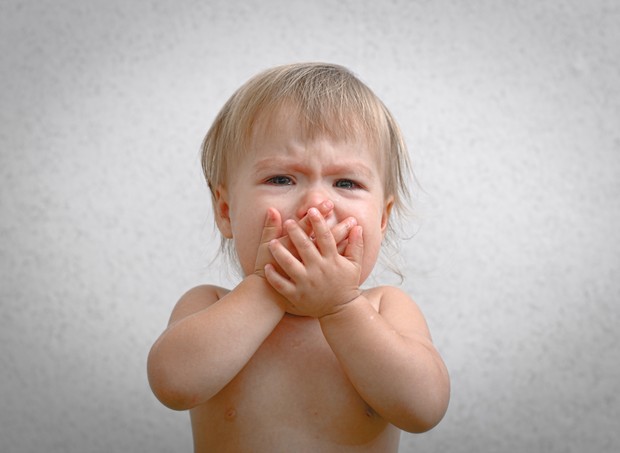 Bebê chorando com a mão na boca (Foto: Thinkstock)