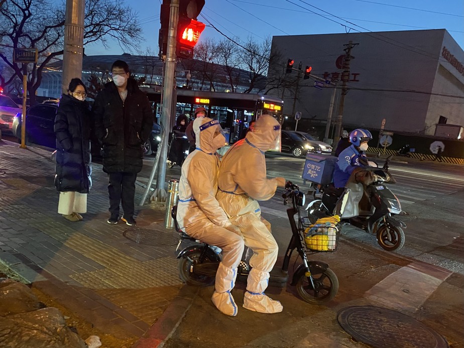 Com roupas protetoras, pessoas andam de bicicleta em Pequim