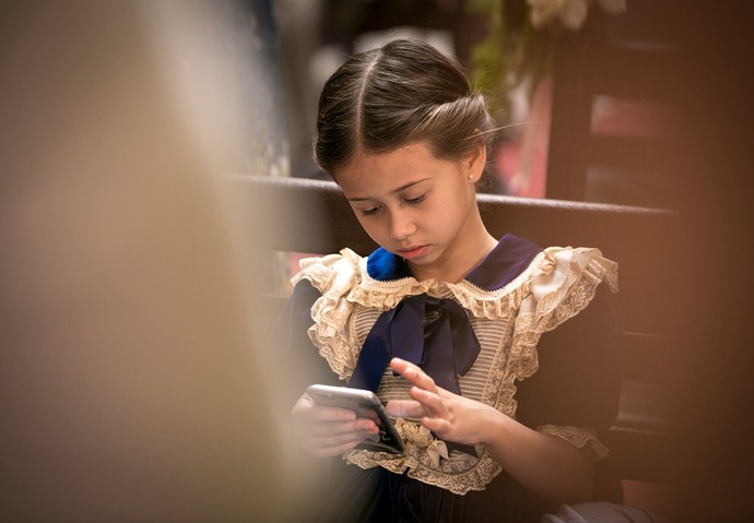 A pequena Nathalia Costa se diverte no celular durante um intervalo na gravação (Foto: Isabella Pinheiro/Gshow)