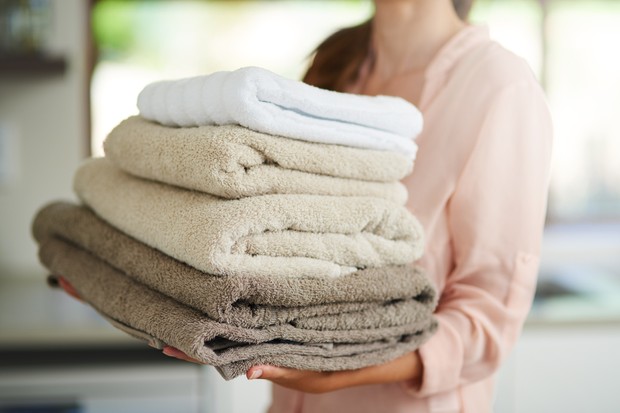 Shot of a young woman carrying a pile of folded towels (Foto: Getty Images/iStockphoto)