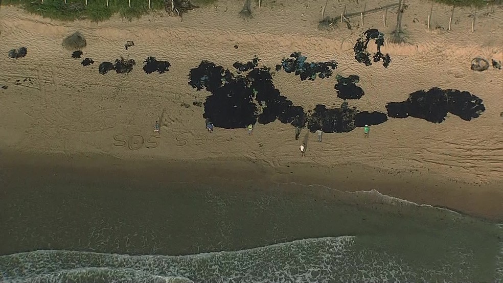 Perto de mancha de óleo na areia, voluntários escrevem 'SOS' em praia do Cabo de Santo Agostinho — Foto: Reprodução/TV Globo