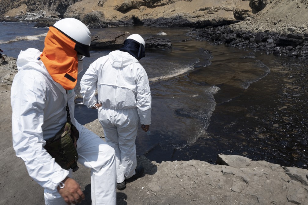 Trabalhadores avaliam área coberta com óleo em praia do Peru em foto de 17 de janeiro de 2022 — Foto: Cris BOURONCLE / AFP