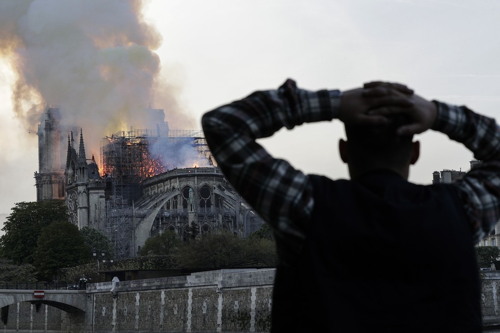 Homem leva as mãos à cabeça enquanto observa o incêndio que consome a Catedral de Notre-Dame, em Paris — Foto: Geoffroy Van Der Hasselt/AFP