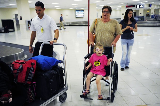 Na foto, Victoria é empurrada em uma cadeira de rodas por Janet Kellum, amiga de sua família, na chegada ao aeroporto de Fort Myers, na Flórida (Foto: Naples Daily News, Corey Perrine/AP)