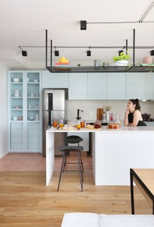 O escritório Studio 92 Arquitetura projetou a cozinha com armários em tom romântico, que contrasta com a prateleira suspensa preta de serralheria e a madeira do piso
