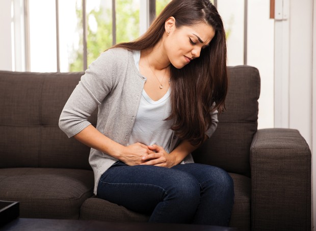 Young Hispanic woman sitting in a couch at home and suffering from colics (Foto: Getty Images/iStockphoto)