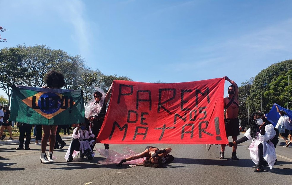 Atores com bandeira do Brasil escrito "luto" fazem performance carregando faixa onde se lê "Parem de nos matar", durante protesto contra Bolsonaro, no DF — Foto: Anna Reis/ TV Globo