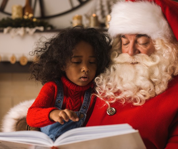 Menina lendo livro no colo do Papai noel (Foto: Thinkstock)