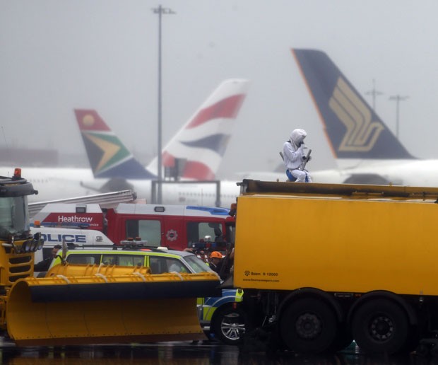 Equipes de emergência conversam com ativista (de branco) que invadiu a pista do aeroporto de Heathrow, em Londres, nesta segunda-feira (13) (Foto: Steve Parsons/PA via AP)