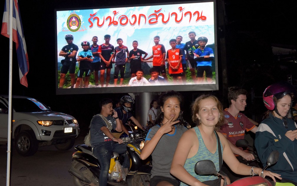 Motoristas passam por cartaz com foto dos integrantes do time Wild Boar e seu técnico com a mensagem “bem-vindos irmãos”, em Chiang Rai, após o resgate do grupo na caverna Tham Luang, na terça-feira (10) (Foto: Tang Chhin Sothy/AFP)