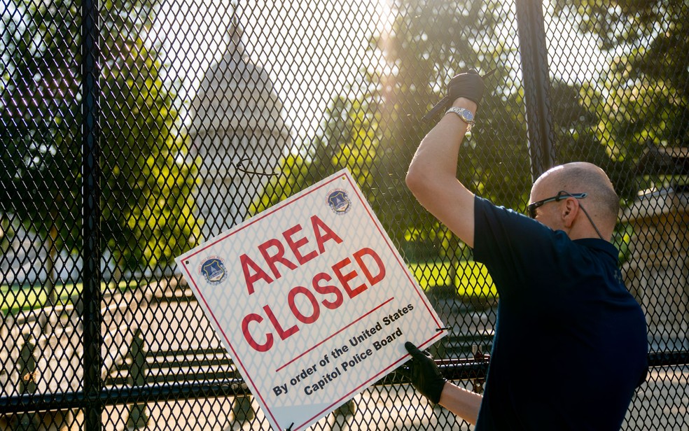 Membro da polícia do Capitólio retira placa de cerca que será removida do local, em Washington DC — Foto: AP Photo/Andrew Harnik