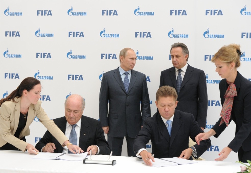 Em foto de 2013, o então presidente da Fifa, Joseph Blatter, e o presidente da Gazprom, Alexey Miller, acertam patrocínio da empresa na Copa de 2018 diante do presidente russo, Vladimir Putin. (Foto: Divulgação)