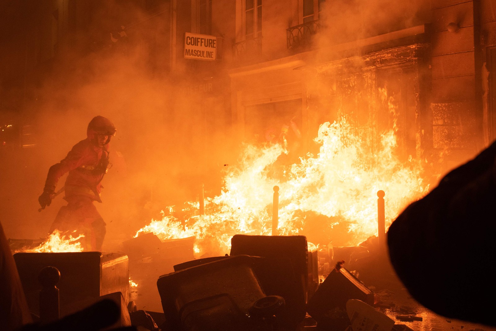 Bombeiro tenta apagar incêndio durante manifestação em Paris uma semana depois de o governo francês ter aprovado uma reforma da previdência no parlamento sem votação — Foto: ANNA KURTH/AFP