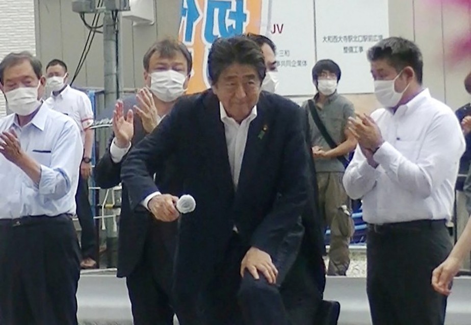 O ex-primeiro-ministro do Japão Shinzo Abe durante o comício onde foi assassinado nesta sexta-feira. O homem ao fundo de camisa cinza é o suspeito de cometer o atentado