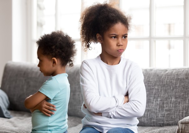 Stubborn small African American brother and sister sit on couch back to back avoid talking, offended mixed race siblings boy and girl with arms crossed angry after fight not speaking to each other (Foto: Getty Images/iStockphoto)