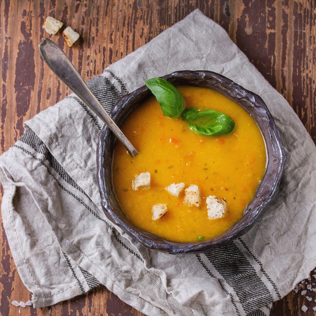 Ceramic bowl of carrot soup, served with fresh basil, croutons, kitchen towel and spoon on old wooden background. Dark rustic style, top view. (Photo by: Natasha Breen/REDA&CO/Universal Images Group via Getty Images) (Foto: Universal Images Group via Getty)