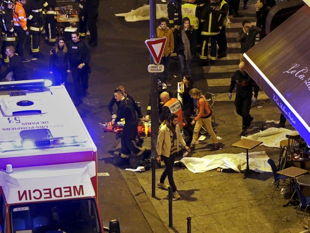 Policiais e bombeiros trabalham ao lado de corpos de vítimas de tiroteio que foram cobertos na calçada em frente a um restaurante de Paris, na França (Foto: Philippe Wojazer/Reuters)