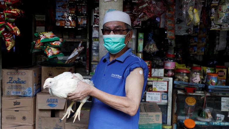 Jeje Jaenudin, 68-year-old local of Sindanglaya village, poses for pictures while holding a live chicken rewarded after receiving his first dose of a COVID-19 vaccine, outside his stall in Cianjur regency, West Java province, Indonesia, June 15, 2021. REU (Foto: REUTERS)