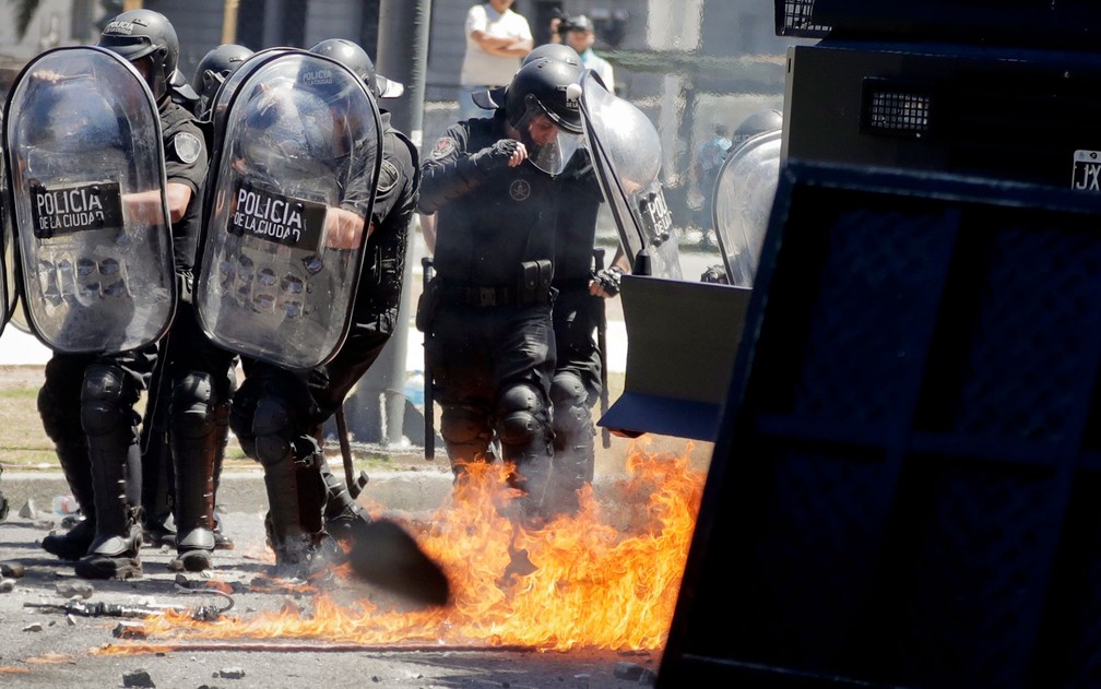 Policiais passam por destroços incendiados por manifestantes durante protesto contra a reforma da previdência em Buenos Aires, na Argentina, na segunda-feira (18) (Foto: AP Photo/Victor R. Caivano)