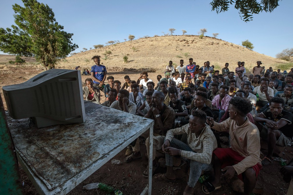 5 de dezembro - Homens que abandonaram região de conflito em Tigray, na Etiópia, se reúnem diante de TV para acompanhar as notícias no campo de refugiados de Umm Rakouba em Qadarif, leste do Sudão — Foto: Nariman El-Mofty/AP